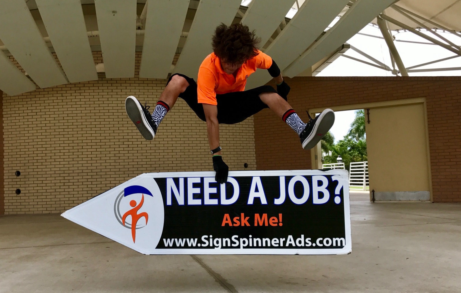 A Spinjas sign spinner jumping over a Need a Job? Ask Me! arrow sign